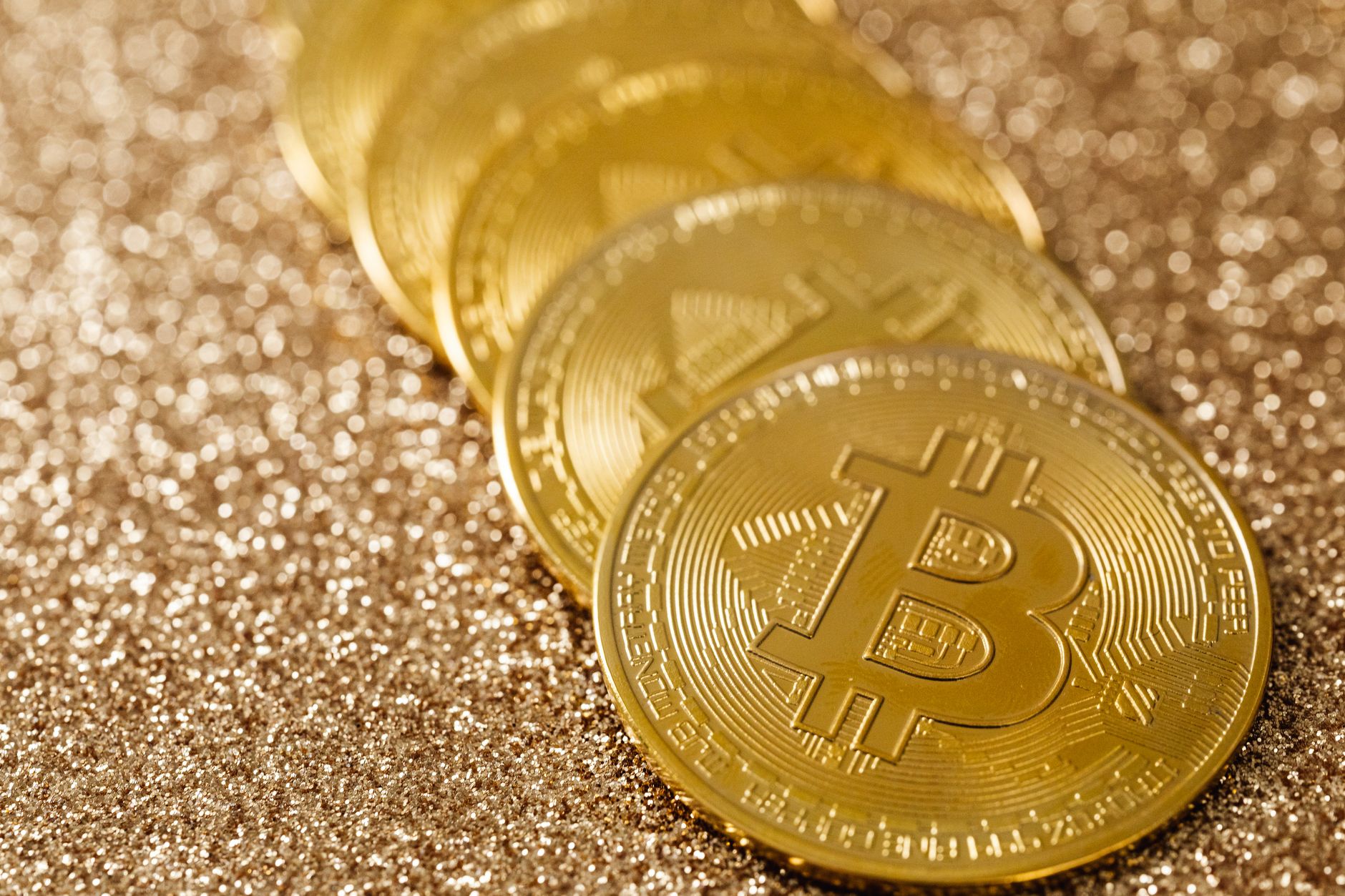 Close-up of golden Bitcoin coins on a shimmering glitter background, symbolizing