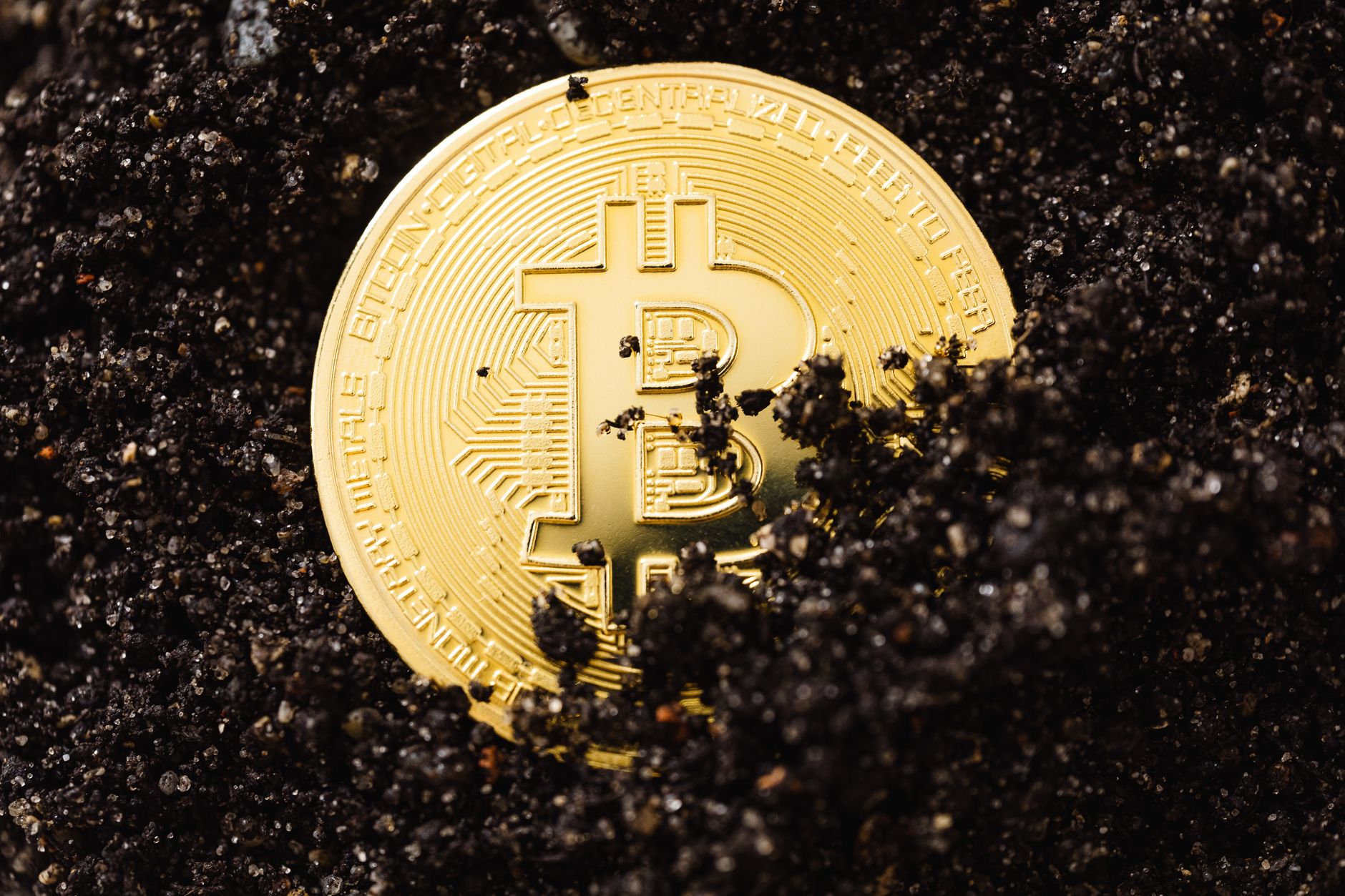 A gold Bitcoin coin partially buried in dark soil symbolizing digital currency g