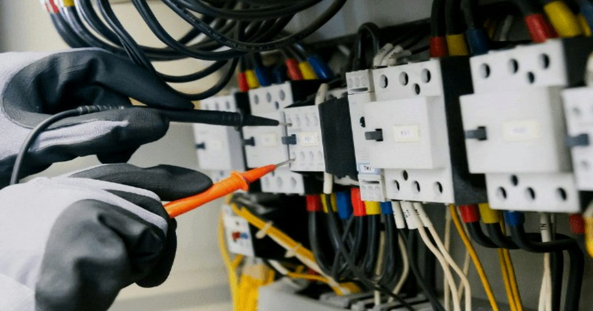 Technician verifying control panel wiring with a multimeter during electrical commissioning