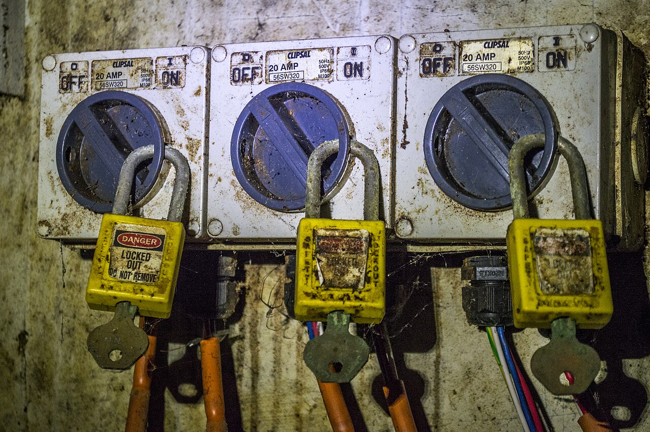 Three industrial isolator switches locked in the off position with yellow danger lockout padlocks