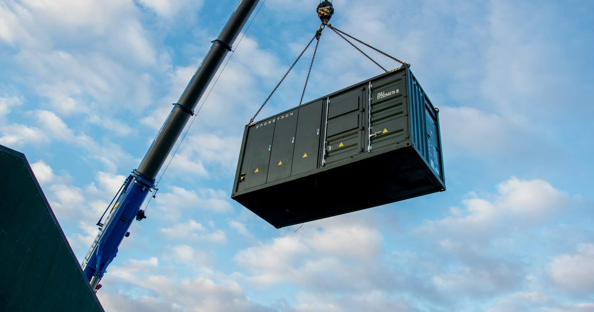 Mobile crane lifting a shipping container by chain slings during a site set
