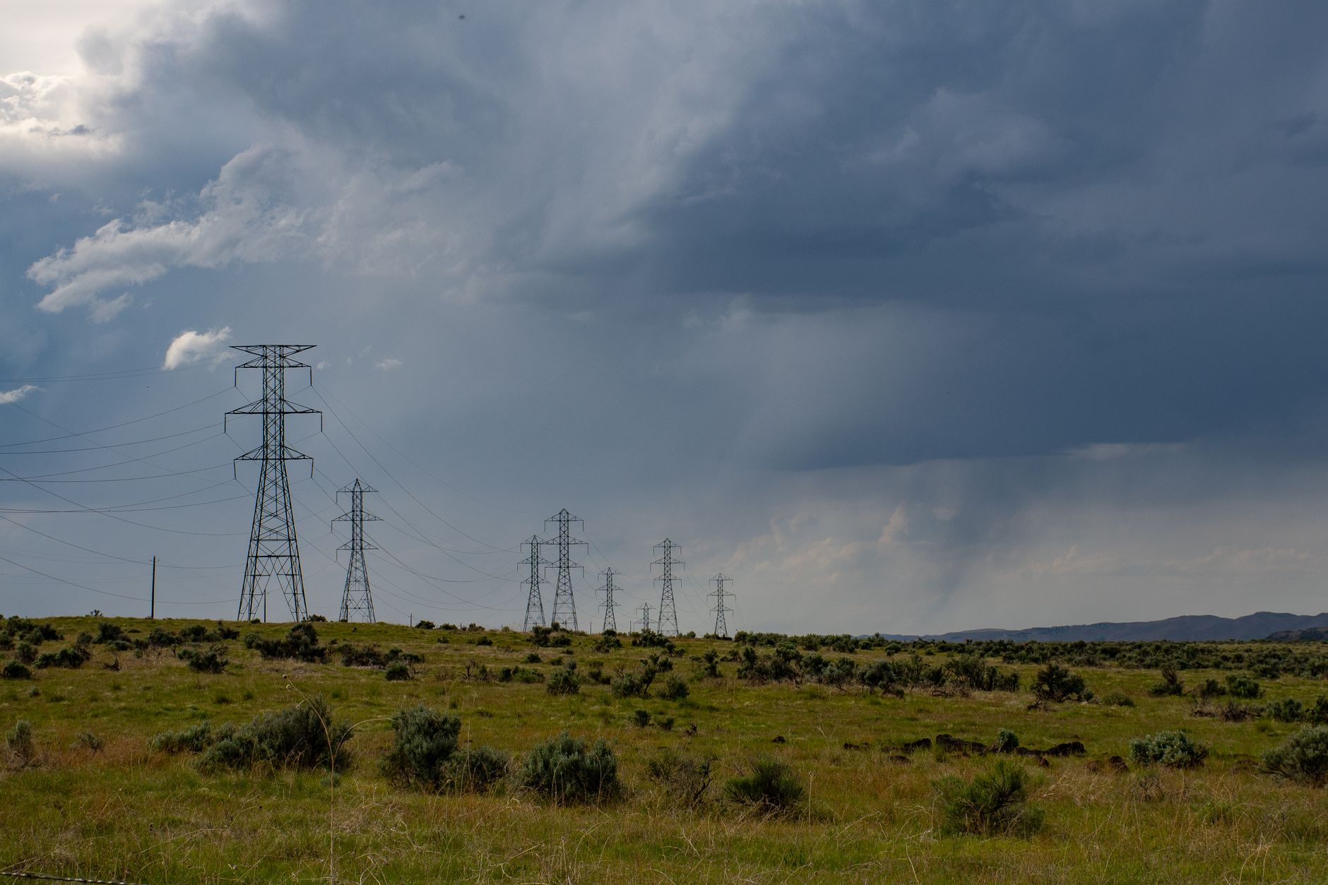 Transmission towers under a dramatic storm sky, illustrating climate and natural disaster risk for bitcoin mining facility site selection