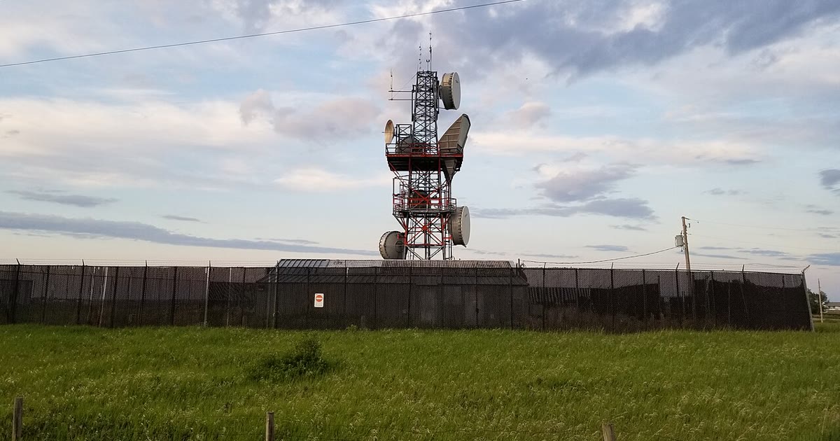 Microwave relay tower with drum antennas at a fenced remote site